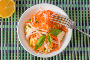 Vegetarian appetizer - Salad with radish daikon with apples and carrots in a bowl and a fork on a bamboo napkin