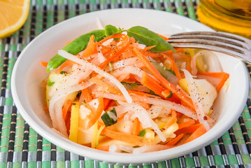Vegetarian appetizer - Salad with radish daikon with apples and carrots in a bowl and a fork on a bamboo napkin