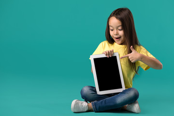 cute little child girl holding blank tablet computer on blue background
