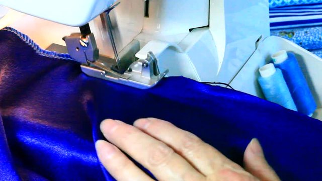 Needlework and sewing at home. Processing of blue satin fabric with a finishing seam on a modern overlock machine