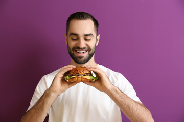 Man eating tasty burger on color background