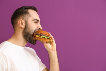 Man eating tasty burger on color background