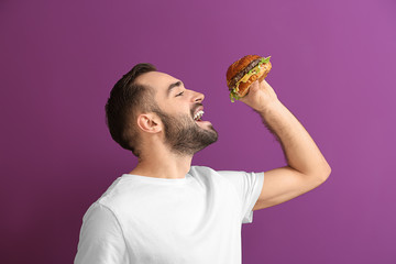 Man eating tasty burger on color background