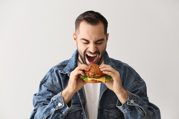 Man eating tasty burger on light background