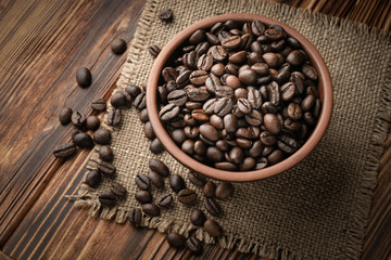 Roasted coffee beans in a clay bowl and scattered on jute cloth on a wooden background
