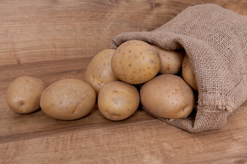 Burlap sack with potatoes on the wooden table.