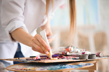 Fototapeta premium Closeup of paintbrush in woman hands mixing paints on palette