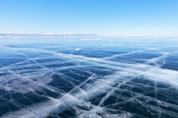 Winter landscape of frozen lake Baikal. The endless fields of smooth blue ice with cracks and snow-capped mountains in the distance. Cold natural background