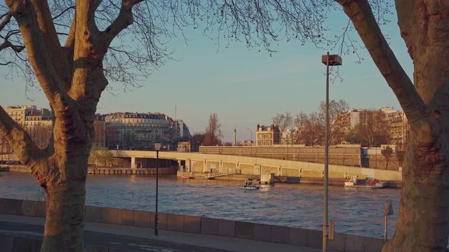 A wide angle of the riverside of the river Seine and the Jupiter Column at la Place de Bastille at sunset in Paris, France. A boat is travelling across the frame.