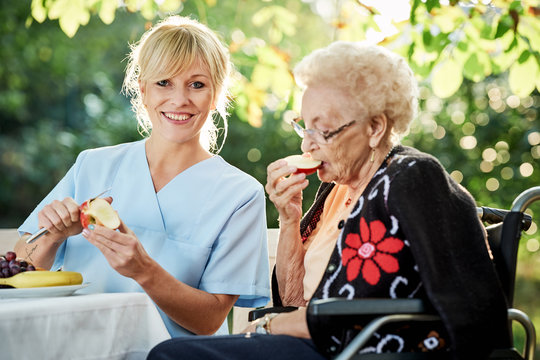 Pflegerin hilft Seniorin beim schälen von Obst