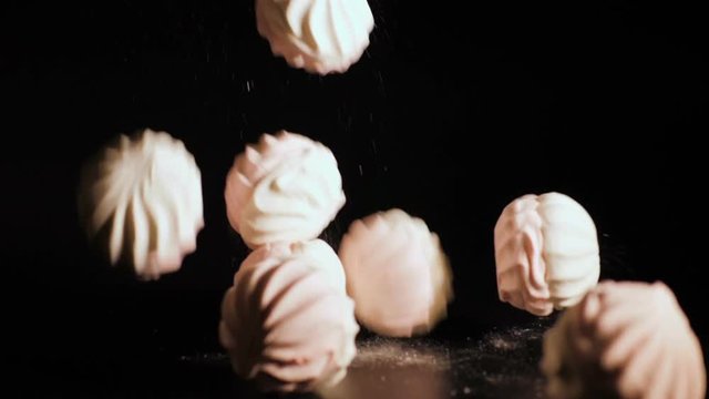 Zefir falling close up. White pieces of marshmallow fall in slow motion a black background and bounce off each other. Closeup.