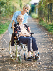 Pflegerin ist mit Seniorin im Rollstuhl am Nachmittag unterwegs.
