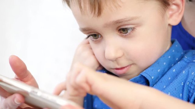 Close-up portrait of a happy smiling boy. Mom and baby play with a smartphone. The child touches the touch screen of the phone with his finger.