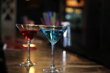 Photography of two martini glasses filled with a colored cocktails standing on the bar counter.