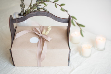 Gift box with spring flowers and candles on light natural fabric background. Easter basket with presents