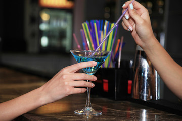 Image of a hand which holds a martini glass on the bar at a nightclub filled with turquoise cocktail.