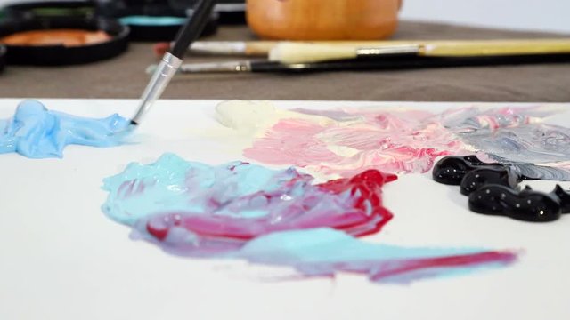 The artist draws a brush with blue paint from the Board for mixing colors and is preparing to paint a picture