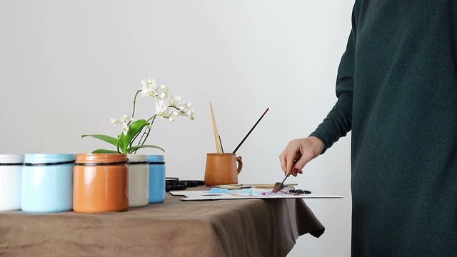 The female hand of the artist, mixes the colors on the Board, and prepares to paint a picture with acrylic paints