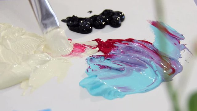 The artist mixes paint brush in ivory and red color palette for mixing colors. Preparing to draw