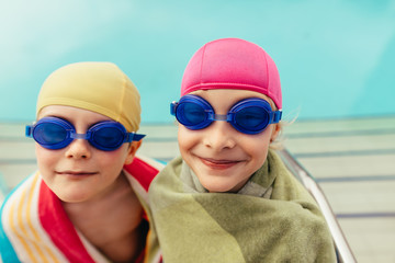Two kids wrapped in towel by poolside