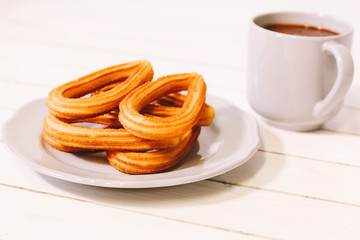 spanish fritters served on white dish on a wooden table with a cup of hot chocolate