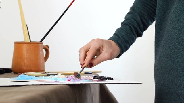 The female hand of the artist, mixes the colors on the Board, and prepares to paint a picture with acrylic paints