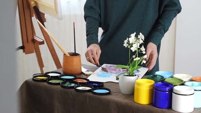 The female hand of the artist, mixes the colors on the Board, and prepares to paint a picture with acrylic paints