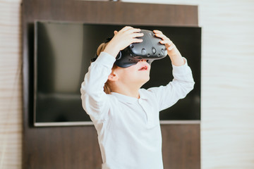 Fototapeta na wymiar The school boy in white shirt wearing virtual reality goggles indoor in living room on background at home.
