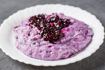 Semolina porridge with blueberry jam in white plate on Dark grey black slate background