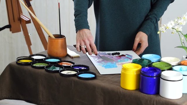 The female hand of the artist, mixes the colors on the Board, and prepares to paint a picture with acrylic paints