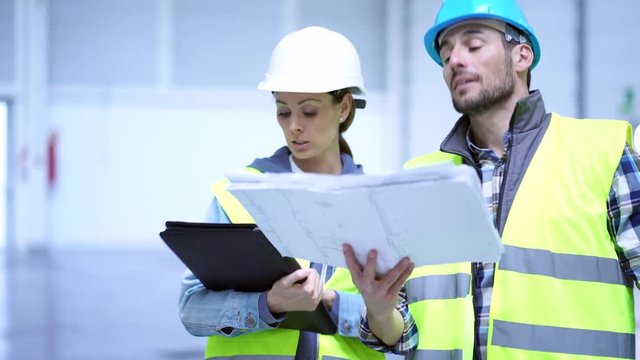 Male and female construction wokers looking over blueprint in empty warehouse