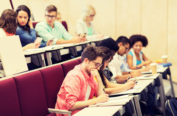 education, high school, university, learning and people concept - group of international students with notebooks writing in lecture hall and talking