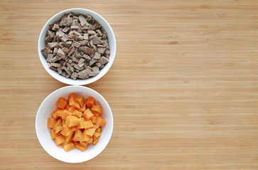 Chopped of boiled pork liver and sweet potato in white bowls on wooden board with copy space.