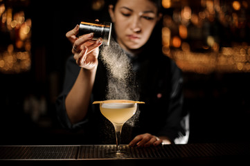 Bartender girl holding a steel spice shaker adding to a delicious cocktail flavours