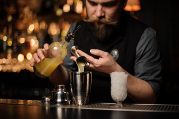 Bartender pouring a delicious alcoholic drink from the steel jigger