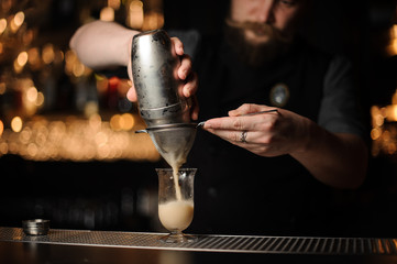 Professional bartender pouring cocktail from the shaker through the sieve