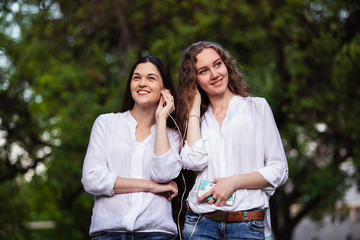 Fototapeta premium Two friends listening to music on headphones in nature. Enjoying your favorite song