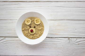 Creative idea for kid breakfast - oatmeal porridge with fruits and berries on a white wooden background . Healthy and fun food for kids.