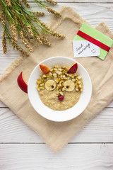 Creative idea for kid breakfast - oatmeal porridge with fruits and berries on a white wooden background . Healthy and fun food for kids.