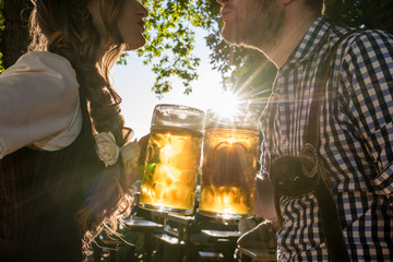 Paar im Biergarten hält Maß Bier in den Händen, Annäherung im Gegenlicht - obrazy, fototapety, plakaty