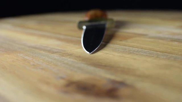 Dagger with wooden handle and two cutting edges rotating on wooden table. Selective focus.