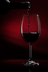 Red wine pouring in a glass from a bottle. Studio shot on black background.