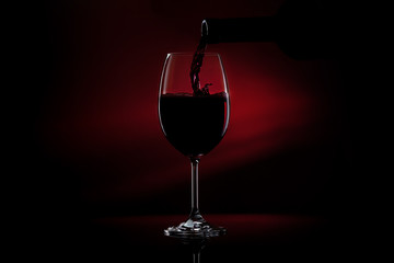 Pouring red wine from a bottle into a wine glass on a black background. Close-up studio shot.