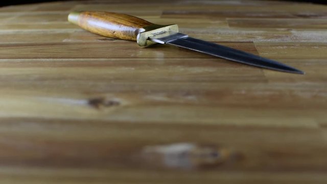 Dagger with wooden handle and two cutting edges rotating on wooden table. Selective focus. Copy space.