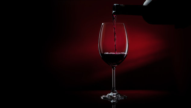 Red wine pouring in a glass from a bottle. Studio shot on black background.