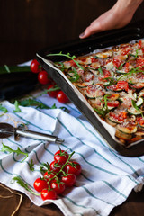 Delicious homemade pizza with tomatoes, eggplants, zucchini, mozzarella parmesan cheese. Decorated with fresh arugula, served on a white towel. Bright colors, smells incredible