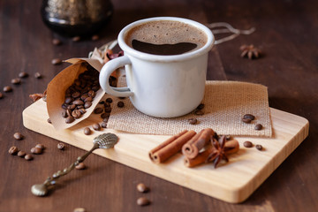 Morning ritual and routine: cup of hot coffee with spices. Lifestyle, good mood for a good day. Coffee beans in a craft paper cornet, anise and cinnamon on a white wooden board. Vintage spoon as decor