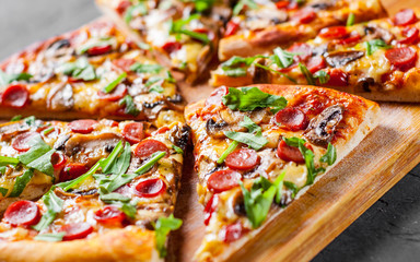 Pizza with Mozzarella cheese, mushrooms, ham, tomato sauce, sausage, pepper, Spices and Fresh arugula. Italian pizza on Dark grey black slate background