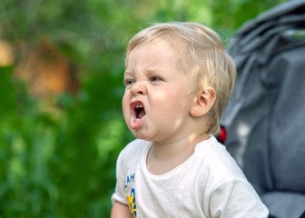 Emotional little boy portrait in the park with green trees on background