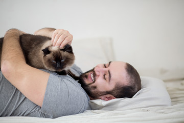 Happy man lying in bed and playing with the cat.